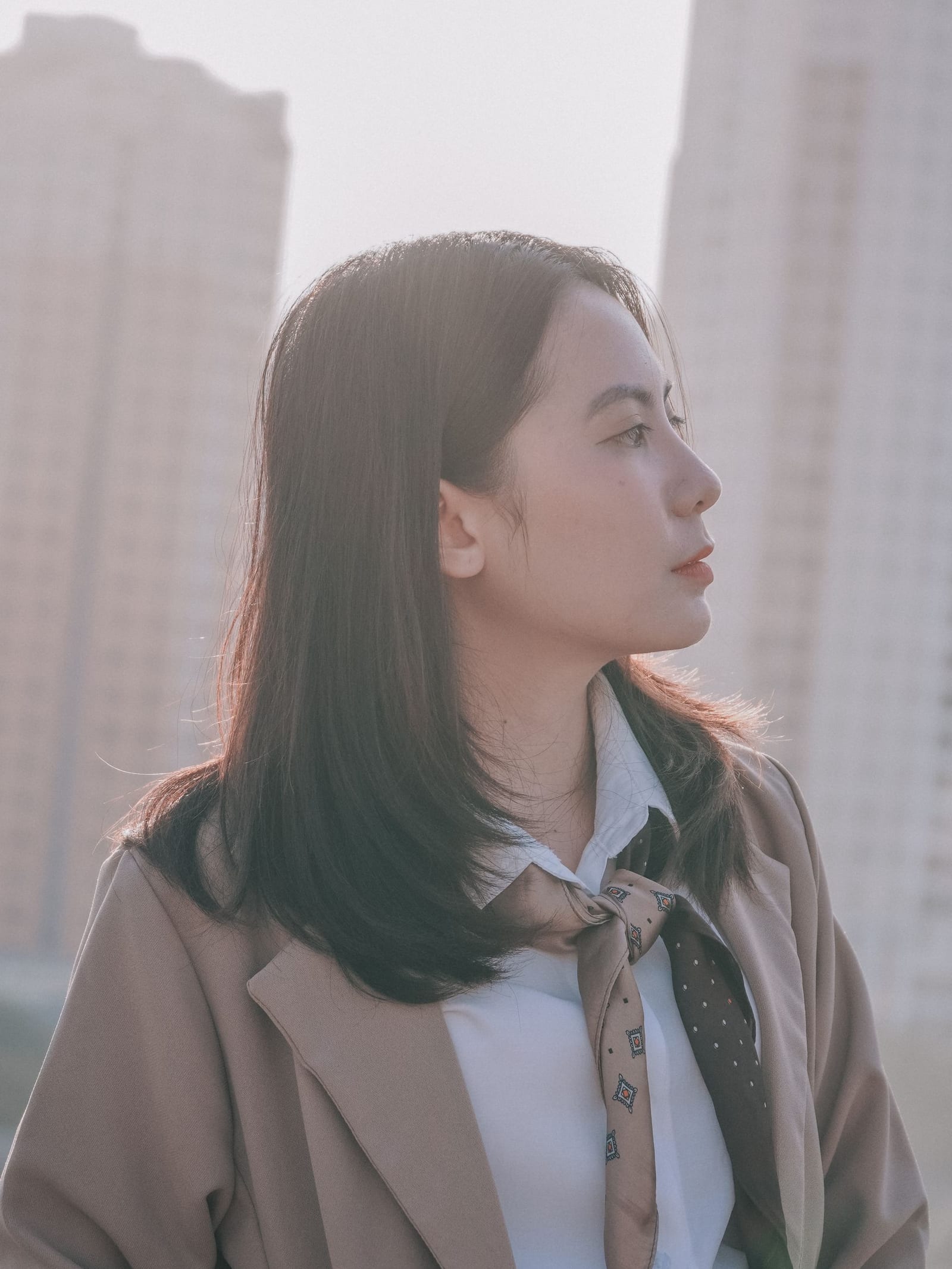 造型八：系丝巾、穿米色西装的女性侧身像，背景是城市楼宇